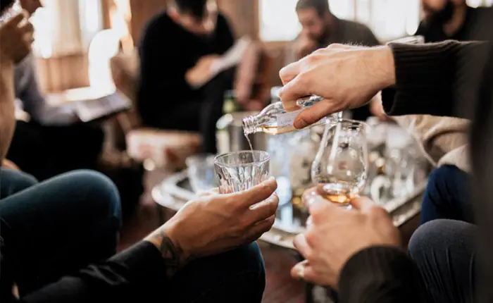 Gesellige Runde bei einem Tasting im Wohnzimmer, fassgelagerte Spirituose wird aus Probe-Fläschchen eingeschenkt
