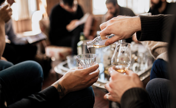 Gesellige Runde bei einem Tasting im Wohnzimmer, fassgelagerte Spirituose wird aus Probe-Fläschchen eingeschenkt